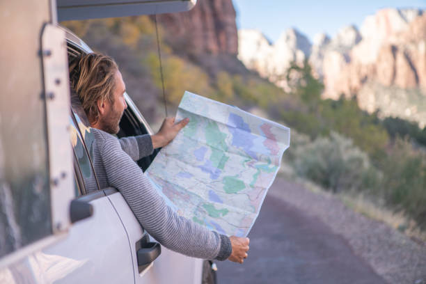 istock Road trip concept; Young man inside campervam looking at road map for directions exploring national parks and nature ready for adventure. 1147701674