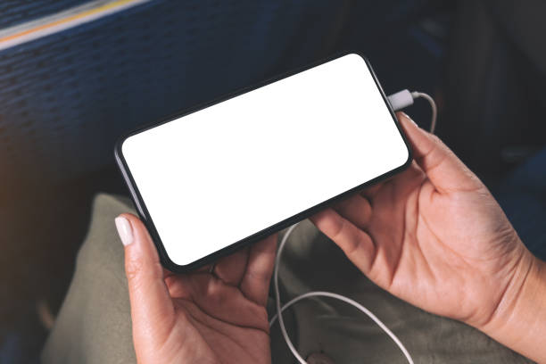 woman's hand holding a black smart phone with blank desktop screen and earphone in cabin Mockup image of woman's hand holding a black smart phone with blank desktop screen and earphone in cabin vehicle interior audio stock pictures, royalty-free photos & images
