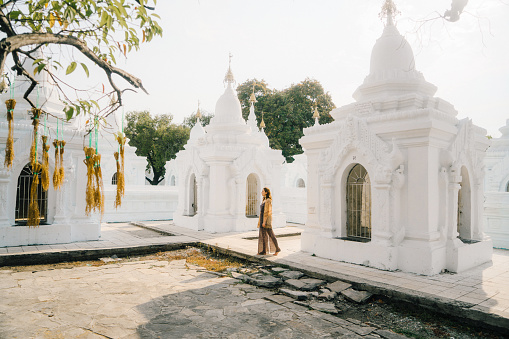 Young Caucasian woman walking in Kuthodaw Pagoda in Mandalay at sunrise, Myanmar