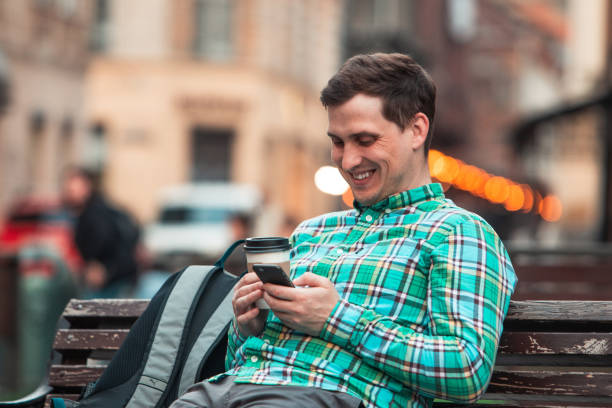istock portrait of young smiling handsome man sitting on bench drinking coffee browsing internet via phone 1147705884