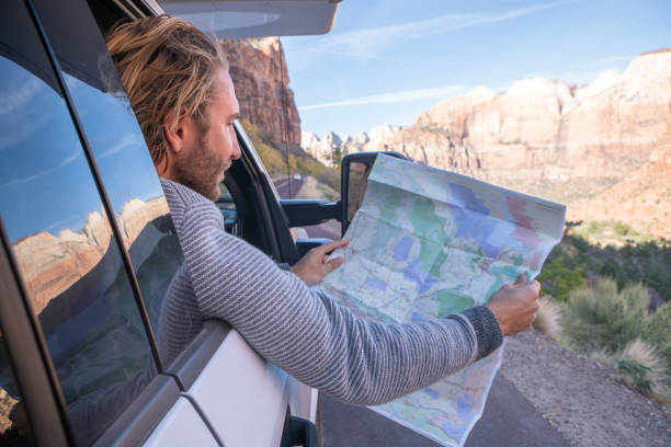 istock Road trip concept; Young man inside campervam looking at road map for directions exploring national parks and nature ready for adventure. 1147706621