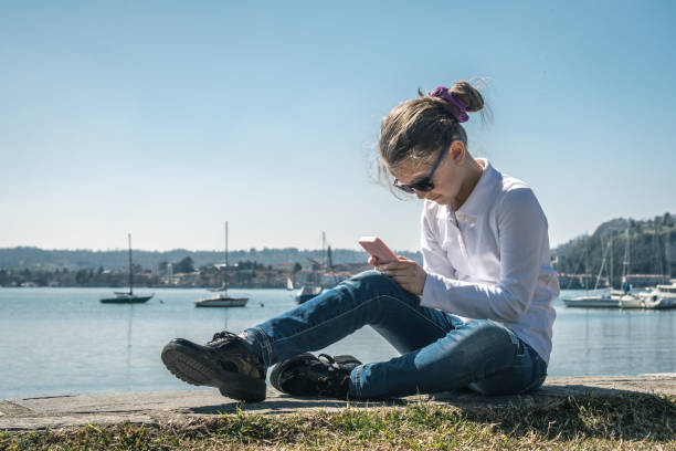 istock Girl Using Mobile Phone While Sitting By Sea Against Sky 1147723174