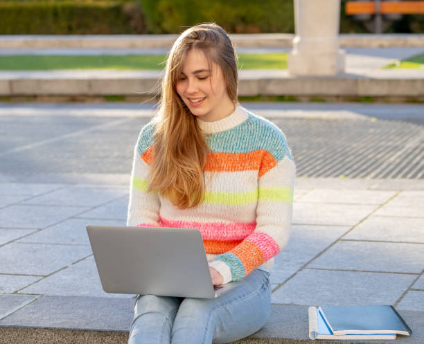 bella giovane allegra adolescente donna che lavora o studia su computer portatile seduto felice e su scale in città all'aperto sfondo urbano. nello stile di vita degli studenti concetto di istruzione e tecnologia online. - surfing the net foto e immagini stock