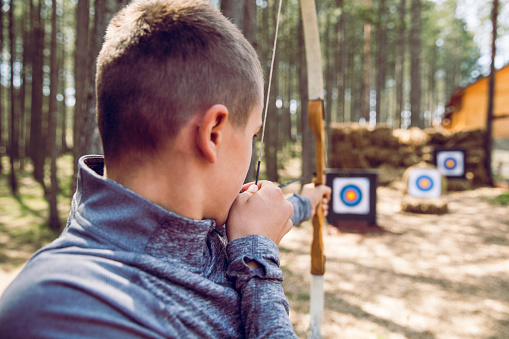 teen boy learning archery at an outdoor park, aiming at a target