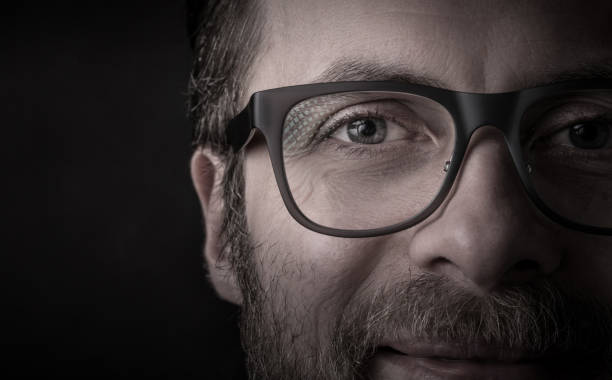Eyes and glasses - happy smiling bearded caucasian man's face close up (macro). Successful businessman portrait on black background, dark moody light. Layout with free text (copy) space.