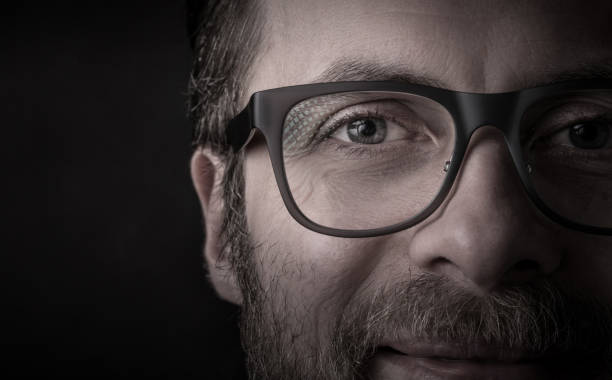 Eyes and glasses - man's face close up (macro) Eyes and glasses - happy smiling bearded caucasian man's face close up (macro). Successful businessman portrait on black background, dark moody light. Layout with free text (copy) space. extreme close up stock pictures, royalty-free photos & images
