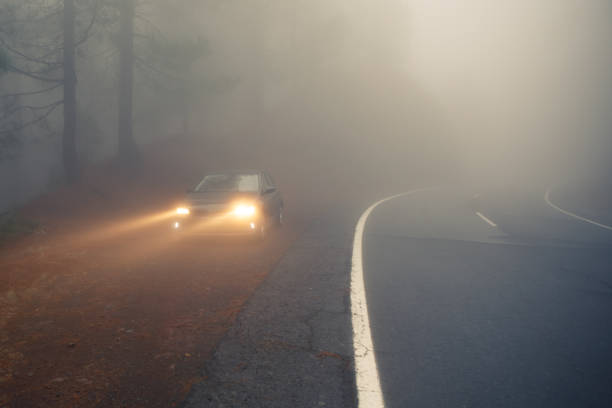 istock dense mist forest road and car on the roadside with light beams 1147738662
