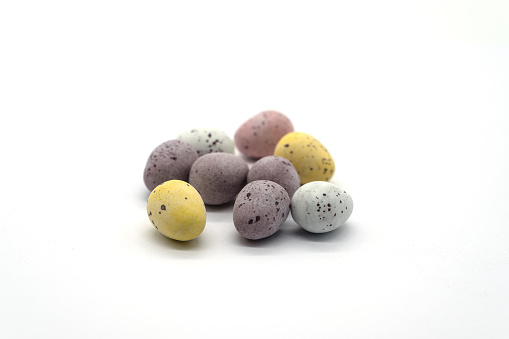 A pile of colourful chocolate eggs on a white background the front egg in focus and the rest softens through the image