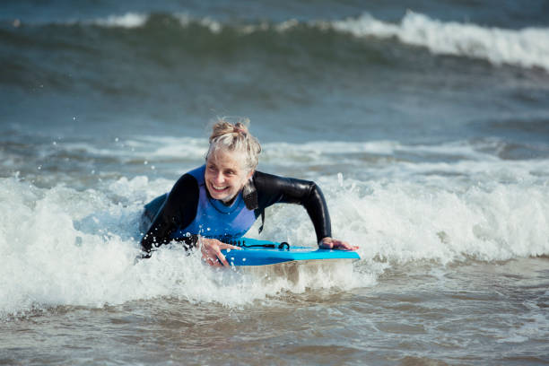 Mature Woman Bodyboarding in the Sea Mature woman having fun on a bodyboard in the sea. body board stock pictures, royalty-free photos & images