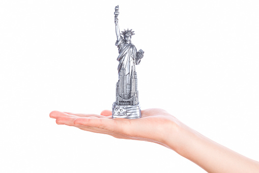 Hand holding a Statue of Liberty souvenir toy on white background. Metal decoration.