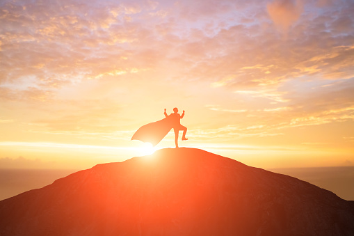 silhouette of super businessman with cape feel excited on the mountain in the sunset