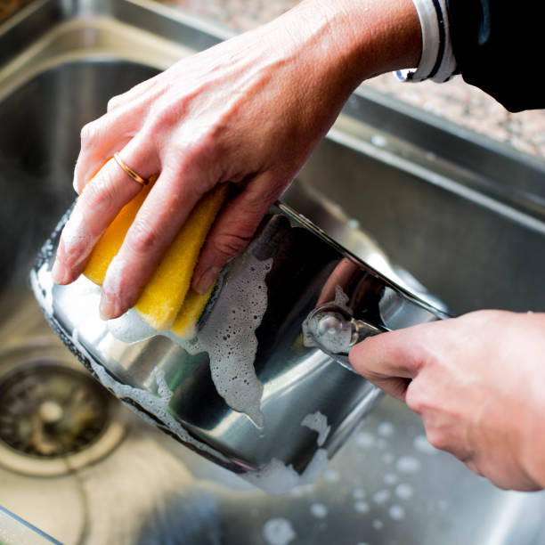 Woman Washing Up a Saucepan in the Kitchen Sink After Cooking