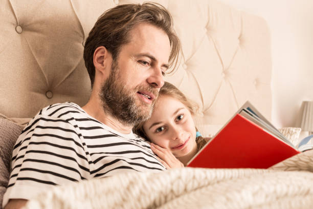 istock Father and daughter reading a book in a bed 1147745585