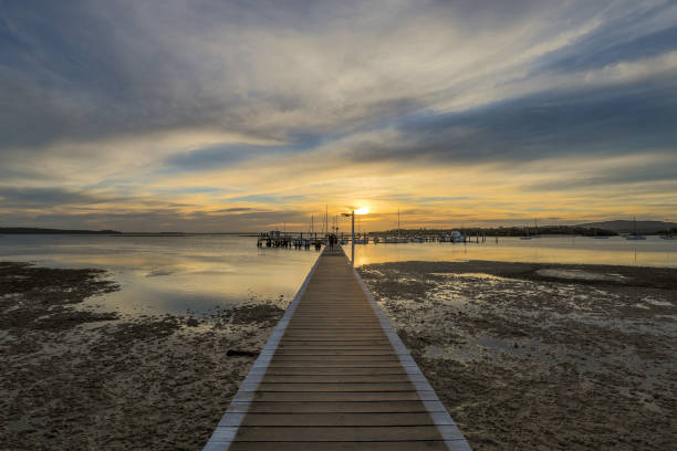 istock Timber jetty leading to sun setting over ocean at low tide 1147747169