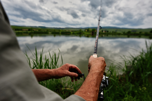 unrecognizable fishing man at the edge of lake enjoying retirement activities.