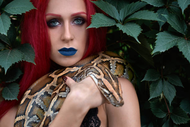 istock Woman with red hair, blue lips posing with big snake. 1147758410