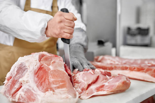 Close up of raw meat and butcher cutting meat with knife. stock photo