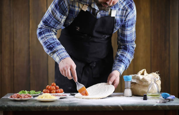 istock man preparing a pizza, knead the dough and puts ingredients 1147763869