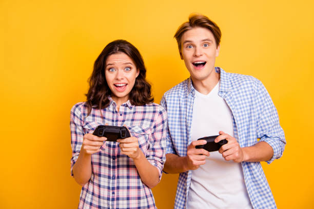 fermez la photo de la paire dans l’amour lui lui son elle son garçon de dame avec des jeux de jeu avec des consoles dans les mains portant casual chemises à carreaux tenue isolé sur fond jaune - pair couple love humor photos et images de collection