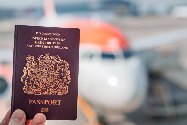 un passaporto rosso britannico trattenuto sullo sfondo di un aereo generico in una luminosa giornata di sole - heathrow airport immagine foto e immagini stock