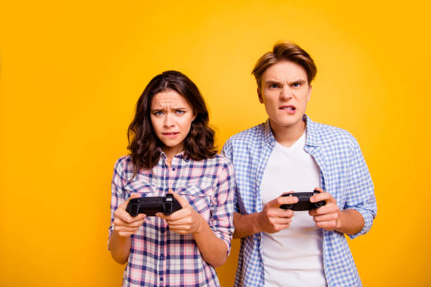 Close up photo of pair in frustration he him his she her lady guy with consoles in hands lost outraged insane wearing casual plaid shirts outfit isolated on yellow background Close up photo of pair in frustration he him his she her lady guy with consoles in hands lost outraged insane wearing casual plaid shirts outfit isolated on yellow background. cross match stock pictures, royalty-free photos & images