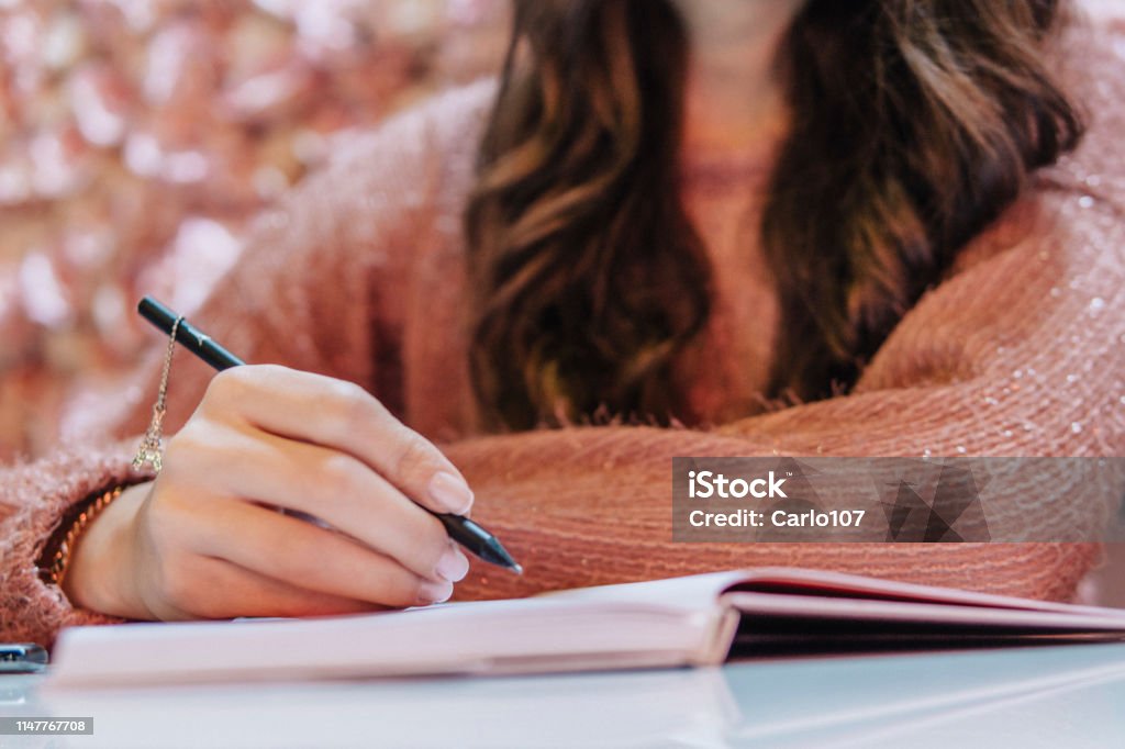 Writing Young woman handwriting on her diary. Pink roses on the background Writing - Activity Stock Photo