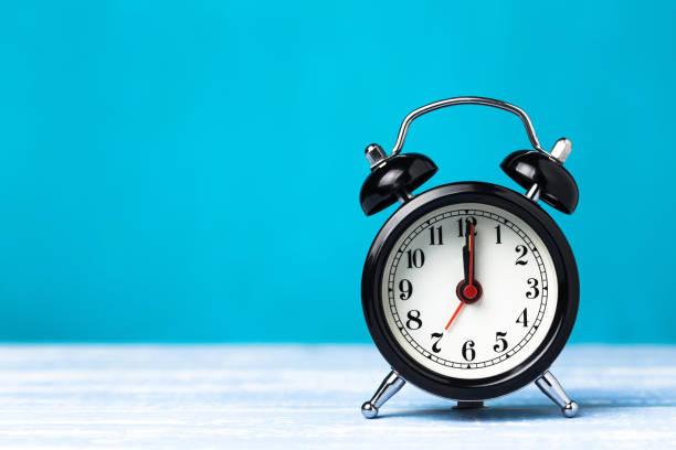 istock Retro black alarm clock on blue background with copy space. Alarm at 7 o'clock clock hand at 12 o'clock 1147768886