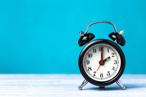 istock Retro black alarm clock on blue background with copy space. Alarm at 7 o'clock clock hand at 2 o'clock 1147768893