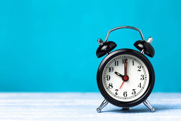 istock Retro black alarm clock on blue background with copy space. Alarm at 7 o'clock clock hand at 10 o'clock 1147768945