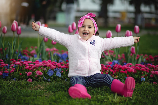 Gorgeous joyful little girl enjoying her time outside near a garden of tulips