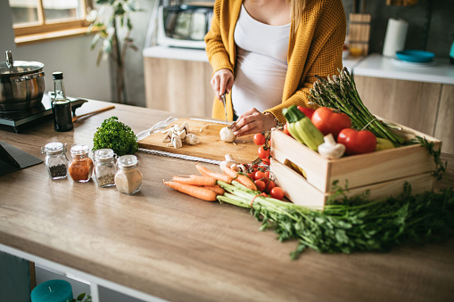 Beautiful pregnant woman following the recipe while cutting mushrooms in the kitchen