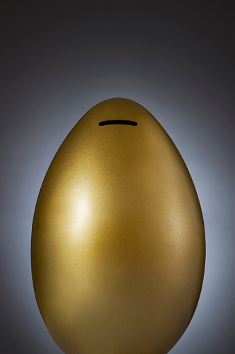 Saving concept with gold colored giant egg coin bank on dark gray background with copy space