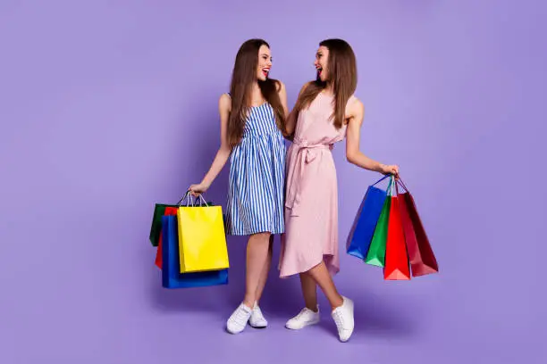 Photo of Full length body size photo two people beautiful she her models chic ladies carry many packs friendly mood laugh laughter wear casual summer colorful dresses isolated purple violet bright background