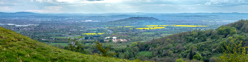 Dramatic high res panorama view over the Cotswold Landscape showing the A417 dual carriageway heading towards Gloucester, patchwork fields of yellow oil seed rape and the distant Malvern hills, shot from Barrow Wake - A high vantage point near the village of Birdlip, high in the Cotswolds