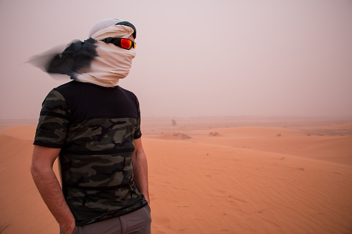 A man with his head covered by a headscarf and sunglasses during a sandstorm in the desert