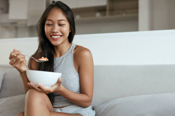 donna sorridente che mangia una sana colazione a casa al mattino - eating women breakfast cereal foto e immagini stock