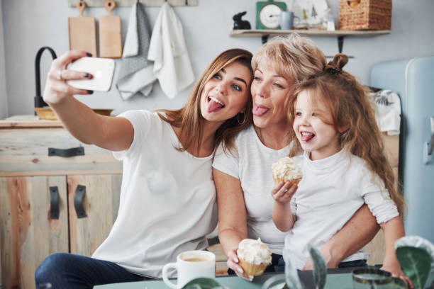 mostra le lingue. madre, nonna e figlia si diverte in cucina - wireless technology cheerful granddaughter grandmother foto e immagini stock