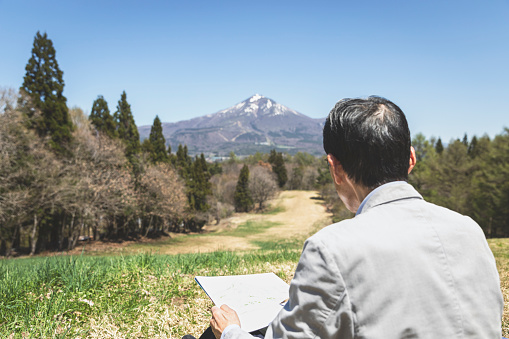 Japanese senior man drawing a picture in the nature.