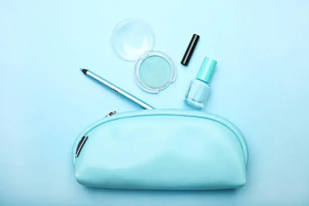 Blue cosmetic bag with set of women's cosmetics on blue background. Concept makeup, make-up artist. Top view.