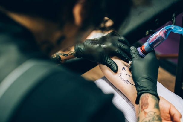 Close up of Tattoo during creation Close up of the female arm with Male tattoo artist tattooing. It is the art work of a wolf, with Native American language script. arm tattoo ideas for men pictures stock pictures, royalty-free photos & images