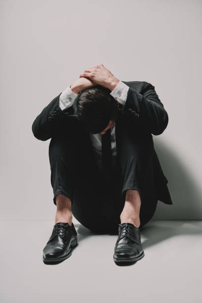 istock Depressed business man sitting on floor head in hands on white background 1147802304