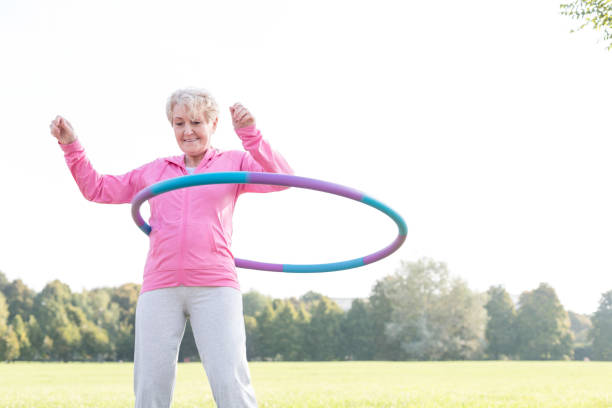 mujer mayor haciendo gimnástica con aro de hula en el parque - hooping fotografías e imágenes de stock