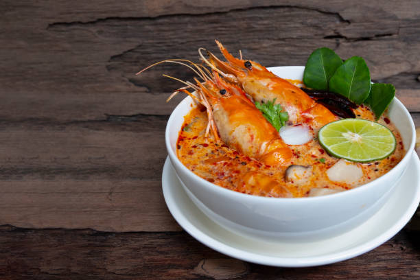 tom yum goong ou soupe aux crevettes épicé soupe aigre la nourriture traditionnelle en thaïlande contient du piment, citronnelle citron vert, feuille de lime, ainsi que du riz cuit dans un plat blanc sur le vieux fond de bois. - sour taste green traditional culture lemon photos et images de collection