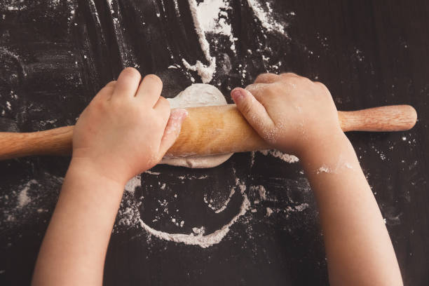 istock hands of a small child palms rolling dough on a brown table with rolling pin, view from above 1147811456