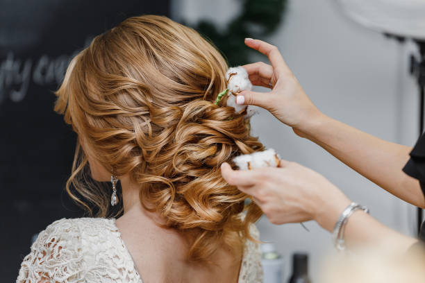 friseur oder blumenhändler macht die braut zu einer hochzeitsfrisur mit frischen baumwollblumen - hair care beauty caucasian preparation stock-fotos und bilder