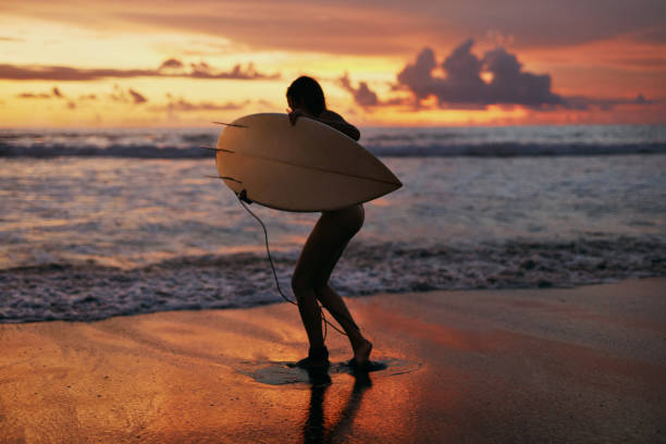 istock Summer. Surfer girl silhouette with surf board on sunset beach 1147812210