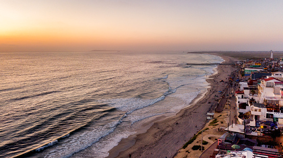 Aerial drone view of the Boardwalk, beach with palapas and umbrellas and the border wall between Tijuana, Mexico, and the United States