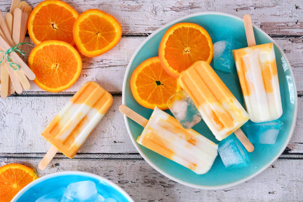 istock Orange yogurt popsicles on a blue plate, top view against white wood 1147819144
