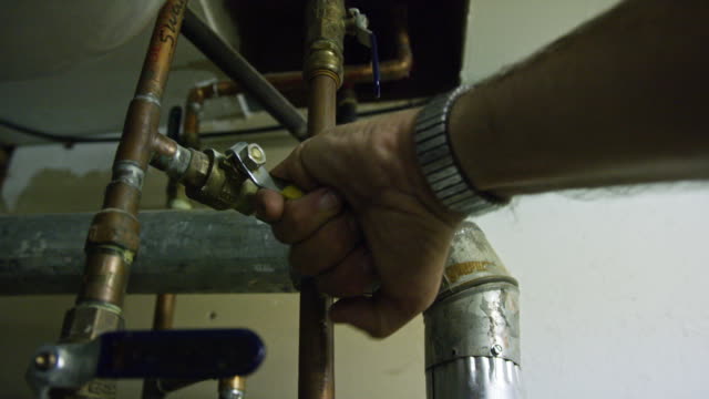 A Caucasian Handyman Turns on the Water for a Swamp Cooler System by Turning a Lever in a Garage Indoors