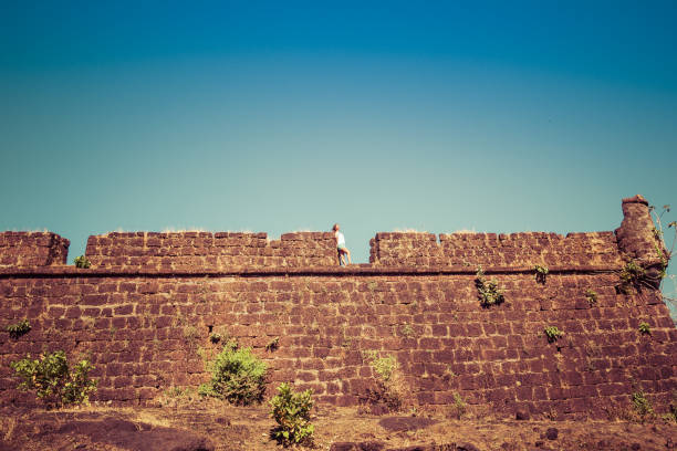 Young woman stands on the brick wall of the old fort Young woman stands on the brick wall of the old fort chapora fort stock pictures, royalty-free photos & images